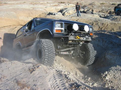 1985 Ford Bronco - A modified Ford Bronco navigates a steep, dusty off-road trail with another vehicle visible in the background.