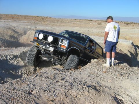 1985 Ford Bronco - Off-road SUV with large tires is stuck in a dirt ditch in a desert landscape.