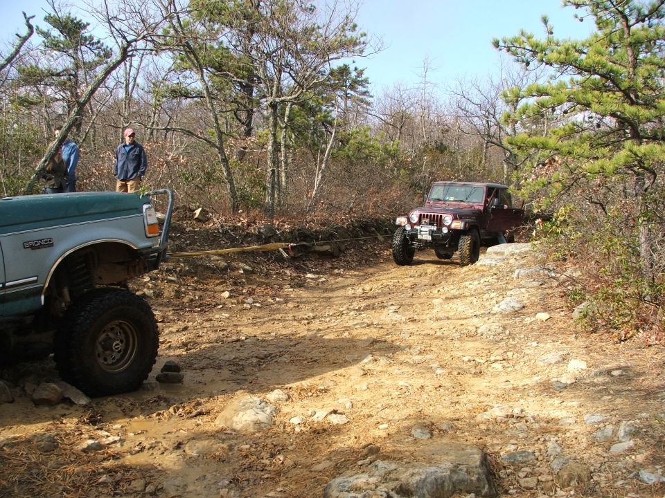 Green 1996 Ford Bronco and red Jeep Wrangler driving on a dirt trail in the woods