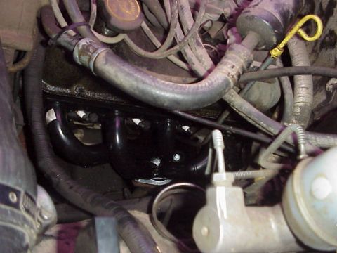 1989 Ford Bronco - Close-up view of engine components, focusing on the exhaust manifold and associated hoses.