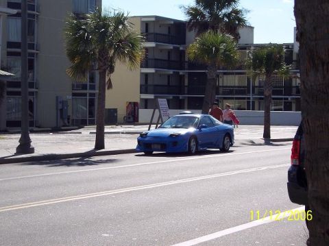 1995 Ford Probe - A blue 1995 Ford Probe is parked curbside on a sunny day, with palm trees and a motel visible behind it.