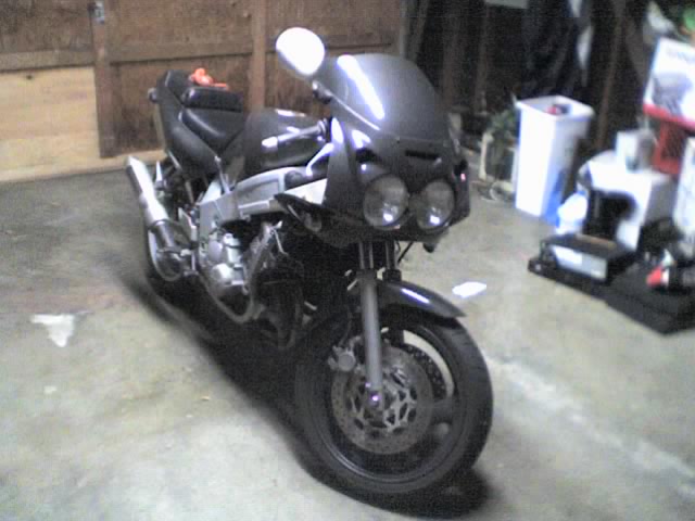 Dark gray sport motorcycle with twin headlights parked in a garage, front three-quarter view