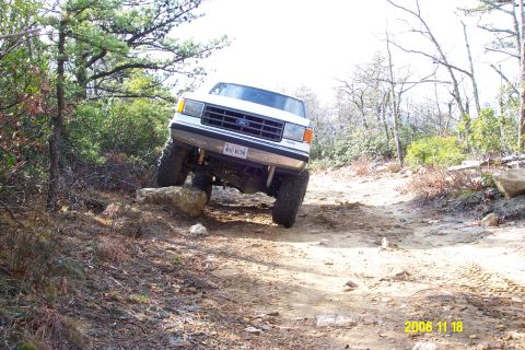 1987 Ford Bronco - White 1987 Ford Bronco navigating a challenging, rocky off-road path.