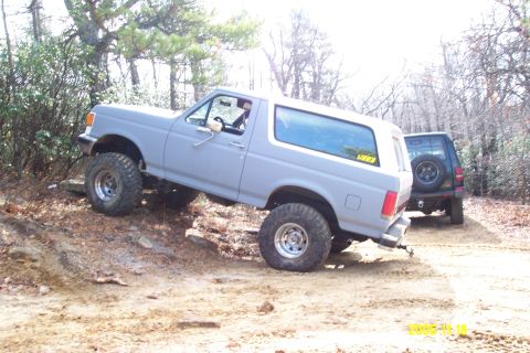 1987 Ford Bronco - Two SUVs, including a 1987 Ford Bronco, navigate a challenging off-road course.