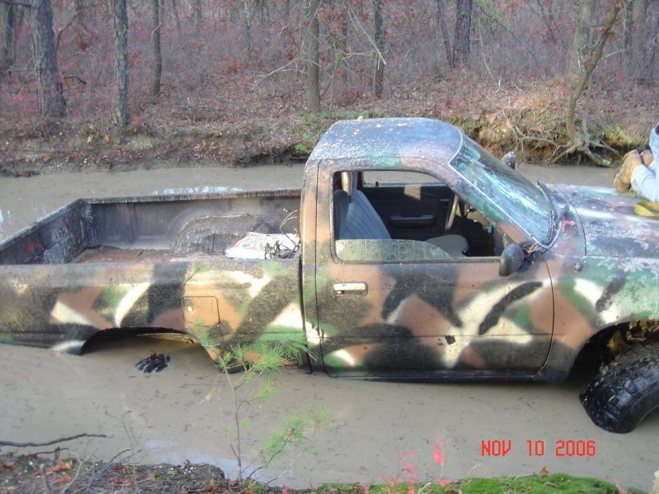 Side view of a camouflaged pickup truck stuck in mud, windshield cracked