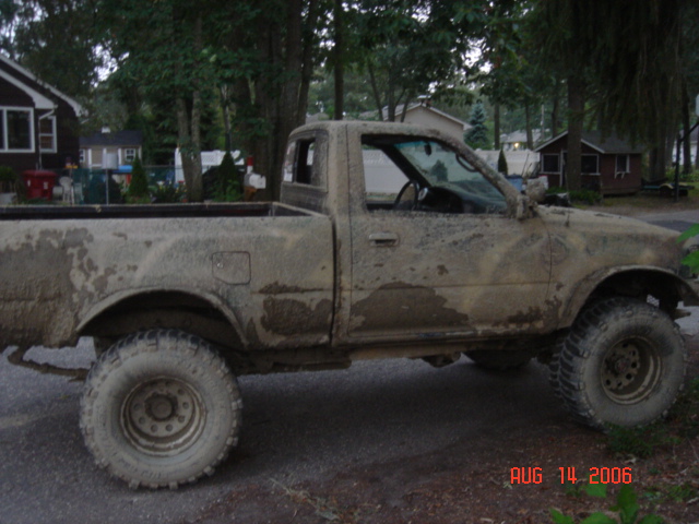 Mud-covered pickup truck, side view, showing its tires and body covered in dirt