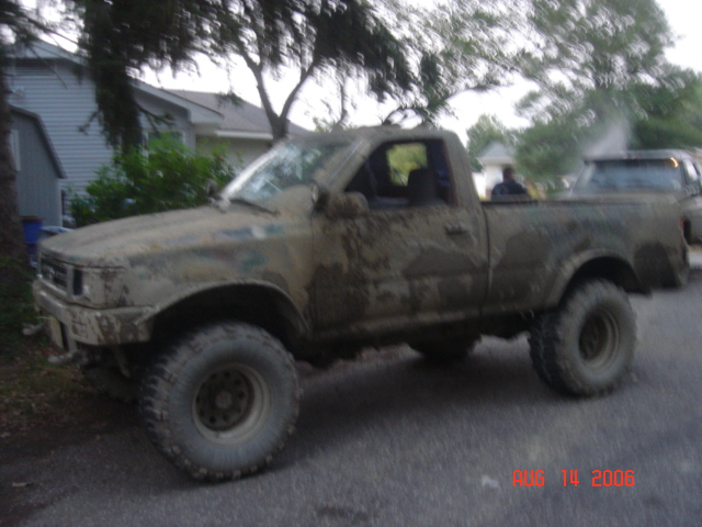 Mud-covered lifted small pickup truck on large tires parked by a house