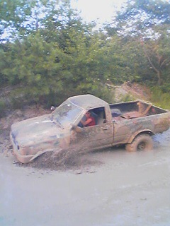 1992 Toyota Tacoma - A muddy Toyota pickup truck is stuck in a ditch, with water splashing around its wheels.