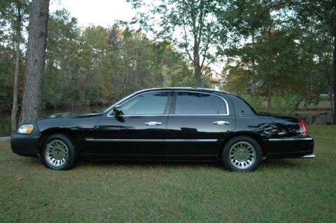1999 Lincoln Town Car - Side profile of a black sedan parked on grass with trees in the background. The body style indicates a late 1990s model.