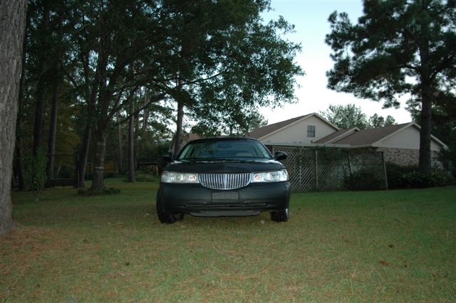 Black sedan with a chrome grille, parked on grass in front of houses