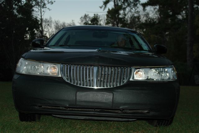 Front view of a dark Lincoln Town Car sedan parked on grass at dusk