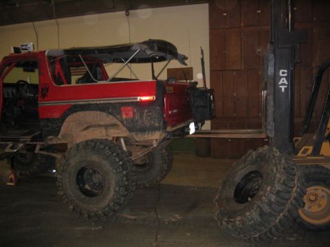 1979 Ford Bronco - A red 1979 Ford Bronco is parked next to a forklift, with its top removed and large off-road tires installed.
