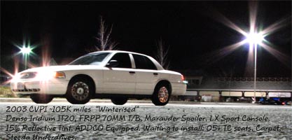 2003 Ford Crown Victoria - A white 2003 Ford Crown Victoria is parked at night, showing its 3q front view with stadium lights in the background.