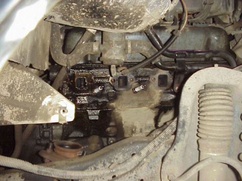 1989 Ford Bronco - Close-up view of an engine's exhaust manifold and spark plugs, showing signs of oil leakage.