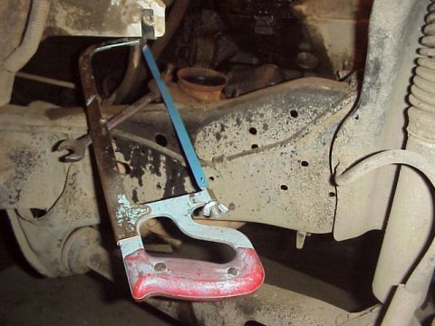 1989 Ford Bronco - A hacksaw is being used to cut into the rusty frame of a vehicle, with suspension components visible.
