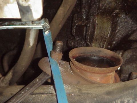 1989 Ford Bronco - Close-up of an exhaust manifold pipe with a blue strap and a wrench, showing mechanical details.