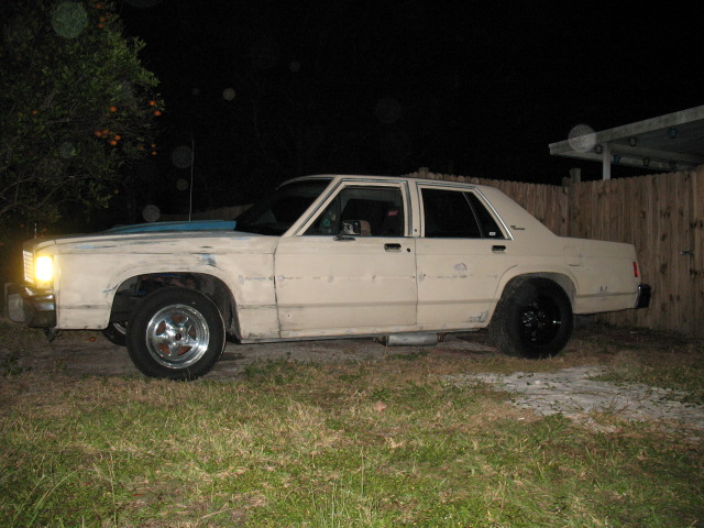 tan sedan with aftermarket wheels and exhaust, parked on grass at night