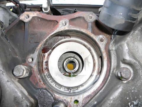 1997 Mercury Grand Marquis - Close-up of the front engine cover with a circular machined coolant passage opening, ringed with rust-colored coolant staining and secured…