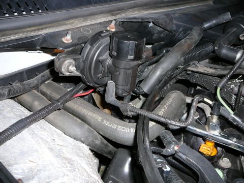 1997 Mercury Grand Marquis - Close-up of an engine bay showing a black plastic secondary air injection or vacuum-operated component mounted near the radiator support, w…
