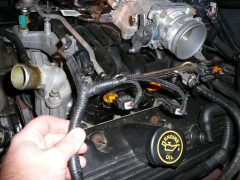 1997 Mercury Grand Marquis - Close-up of an engine bay showing a hand holding a braided fuel injector wiring harness near the fuel injectors and rail; a black 'ENGINE O…