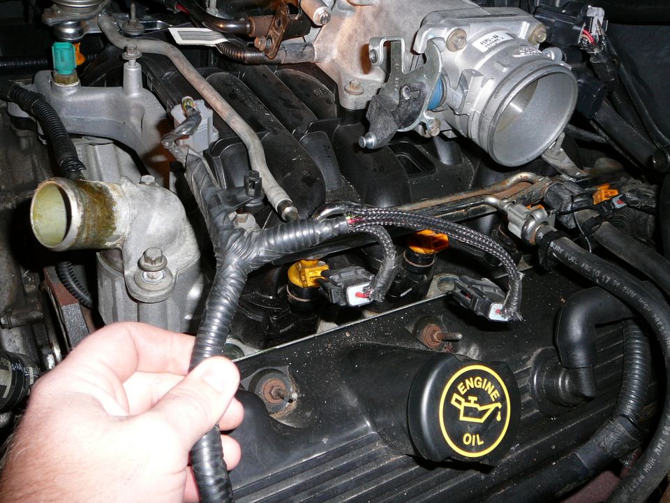 Hand holding fuel injector wiring harness in engine bay near oil filler cap
