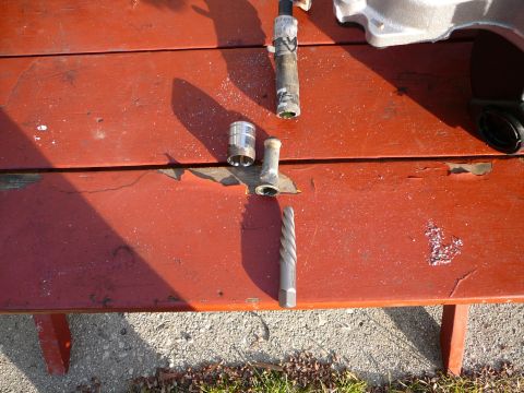 1997 Mercury Grand Marquis - A spiral-flute screw extractor with a hex drive end lies on a weathered red picnic table next to the short brass coolant nipple it backed o…