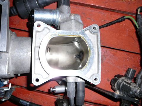 1997 Mercury Grand Marquis - Looking straight into the four-bolt throttle-body flange of a removed cast aluminum intake plenum, showing the smoothed, port-matched inlet…