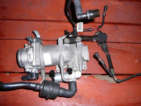 1997 Mercury Grand Marquis - Removed cast aluminum upper intake elbow and throttle body assembly sitting on a red-painted wooden deck, still wearing its Ford Motorcraft…