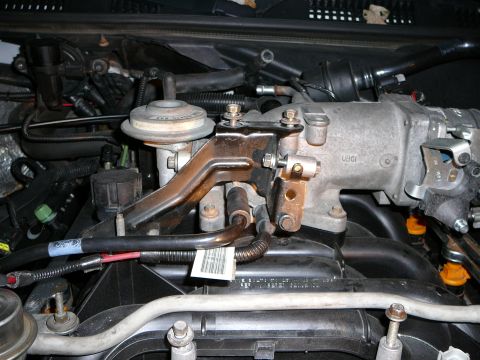 1997 Mercury Grand Marquis - Close-up down into an engine bay at the rear of the intake with the throttle linkage removed, showing the bare bracket, EGR valve and its t…