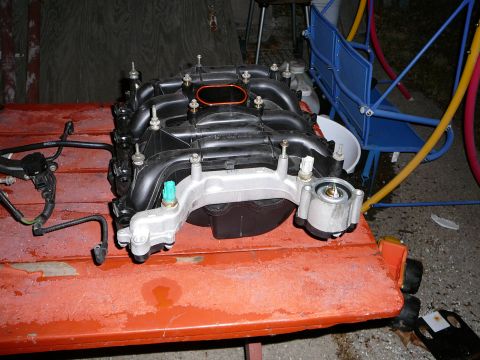 1997 Mercury Grand Marquis - Composite V8 intake manifold removed from the engine and set on an orange creeper or cart, viewed from the front so the aluminum crossover…