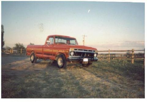 1979 Ford F-150 - Scanned film photo of a red long-bed regular-cab Ford pickup parked on a dirt patch beside a wooden rail fence at sunset, shot from the fro…