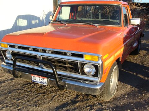 1979 Ford F-150 - Low 3/4 front view of an orange Ford dentside regular-cab long-bed pickup parked on gravel in low sun, showing the chrome FORD-lettered gri…