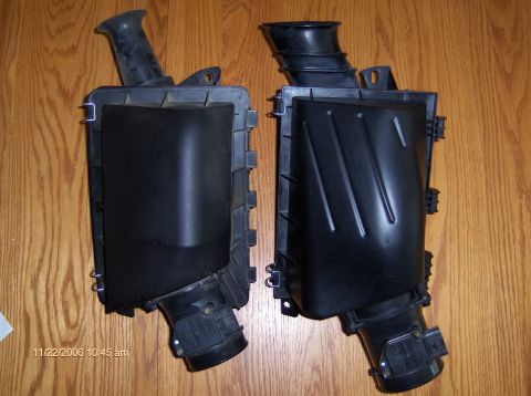 2004 Ford Crown Victoria - Two black plastic air intake boxes are shown against a wooden background, with one a ribbed hose.