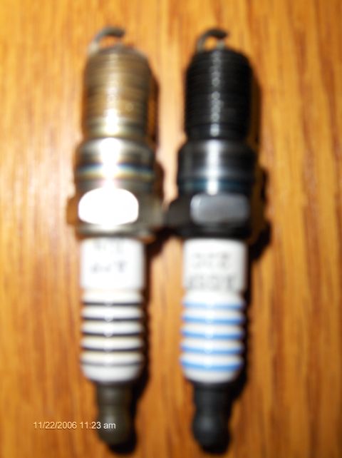 2004 Ford Crown Victoria - Two spark plugs are shown on a wooden background. One appears used, the other new.