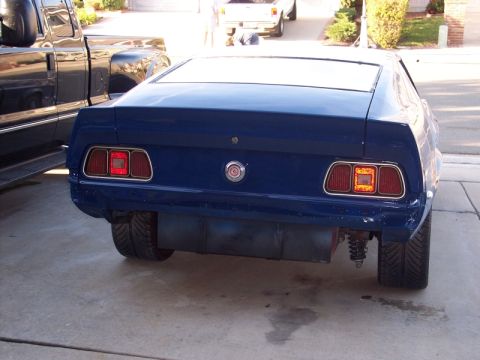 1971 Ford Mustang - The rear of a blue 1971 Ford Mustang is shown, parked next to a black truck. Modifications to the fuel tank and suspension are visible.