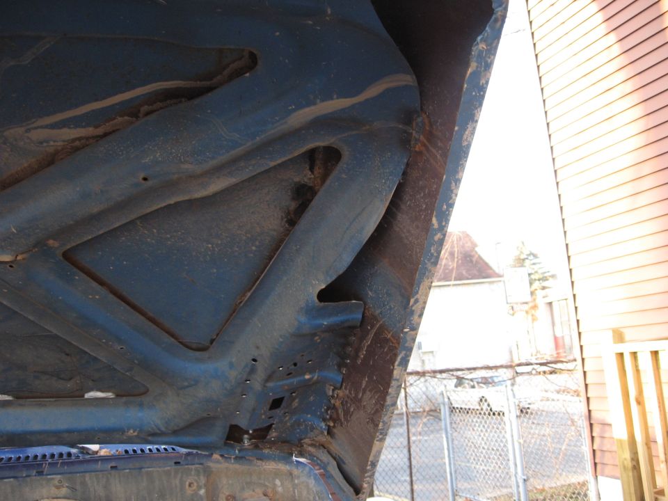 underside of a blue vehicle hood, showing structural supports and some rust
