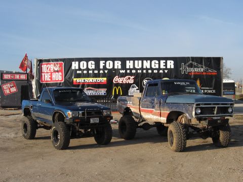 1977 Ford F-150 - Two lifted trucks, a 1977 Ford F-150 and a Toyota, are parked in front of a "Hog for Hunger" banner.