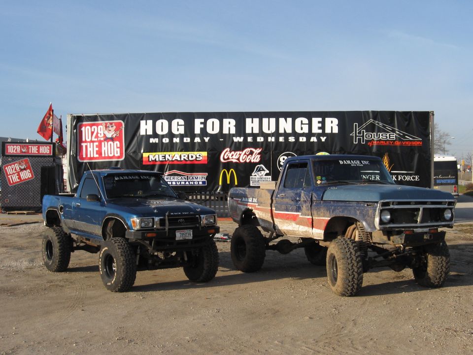 1977 Ford F-150 and a blue Toyota pickup truck parked side-by-side, both heavily modified with lift kits and large tires