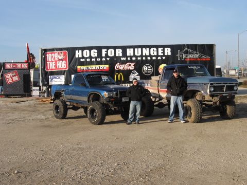 1977 Ford F-150 - Two lifted pickup trucks are parked in front of a 'Hog for Hunger' banner.