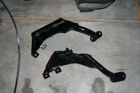 1992 Ford Bronco - Two black suspension brackets are shown on a concrete floor, likely for a vehicle modification project.