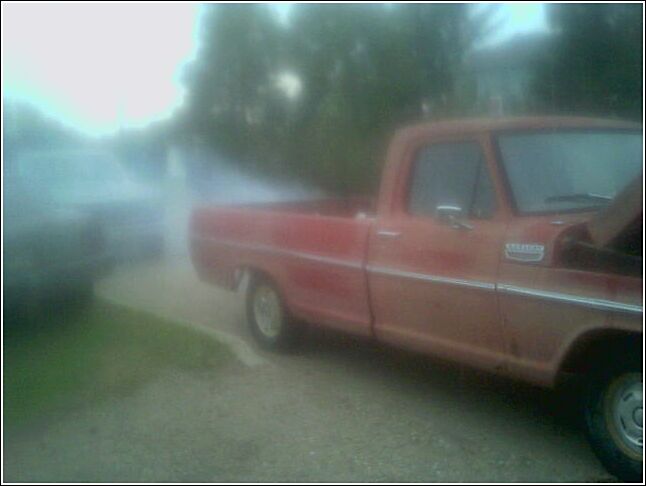 Faded red long-bed classic pickup parked on a gravel drive, blurry side view
