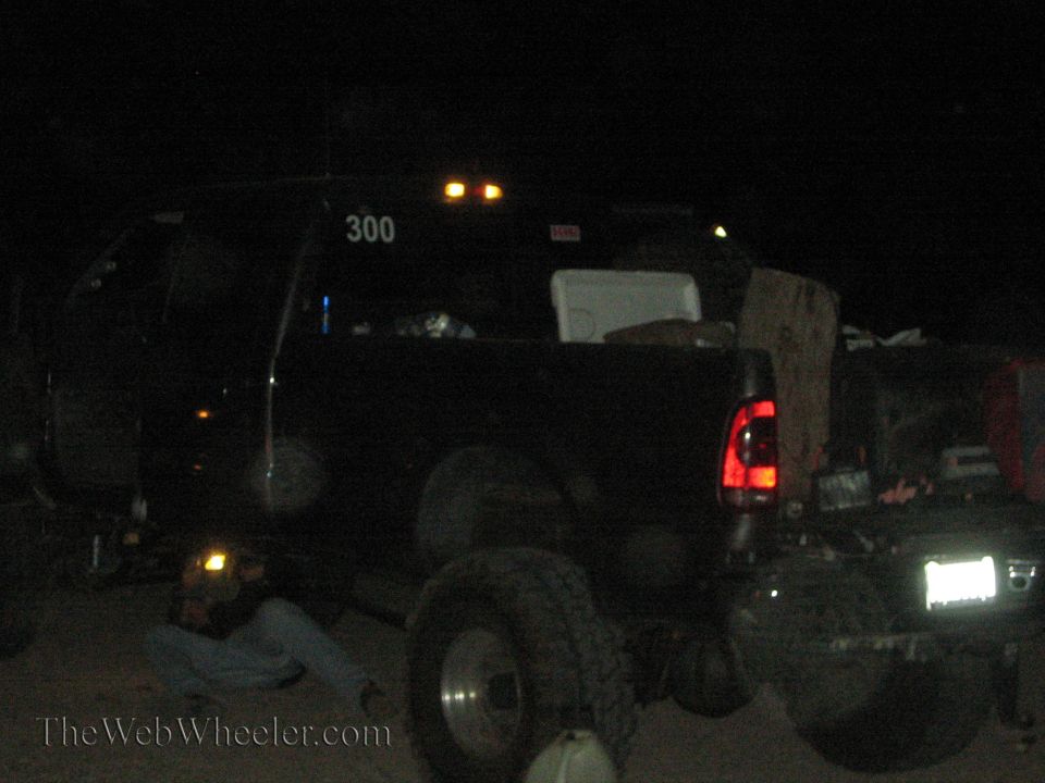 Dark pickup or SUV number 300 being worked on at night with a person underneath