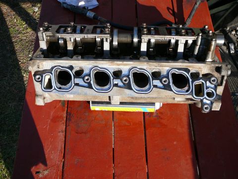 1997 Mercury Grand Marquis - A disassembled engine cylinder head is shown resting on a weathered red table outdoors.