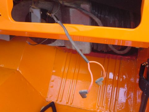 1977 Ford Bronco - Close-up of wiring and connectors inside an orange vehicle, showing the ribbed floor.