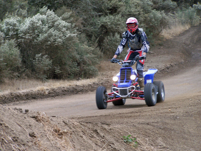 Rider in motocross gear on a blue sport ATV with twin headlights coming down a dirt trail