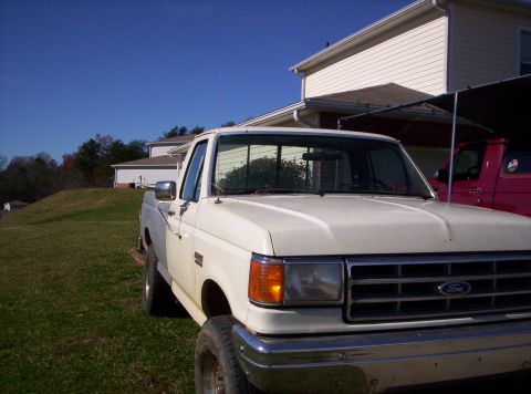 1995 Ford Bronco - A white Ford F-Series truck is parked on a grassy lawn next to a house, with another truck partially visible in the background.