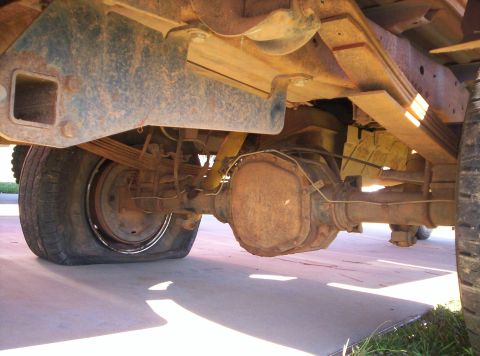1995 Ford Bronco - Underbody shot of a truck's rear axle taken from beneath the driver side, showing the surface-rusted differential housing and cover, leaf s…