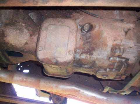 1995 Ford Bronco - The underside of a vehicle reveals a heavily rusted transmission housing and exhaust system.