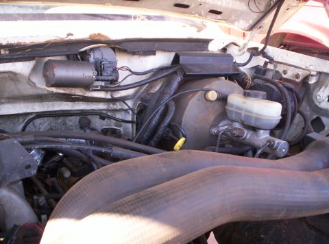 1995 Ford Bronco - Passenger-side engine bay of a white truck showing the round brake booster with master cylinder and translucent fluid reservoir, the yellow…