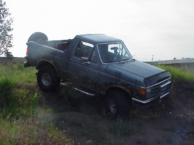 Topless lifted gray Ford Bronco with mural driving through tall grass